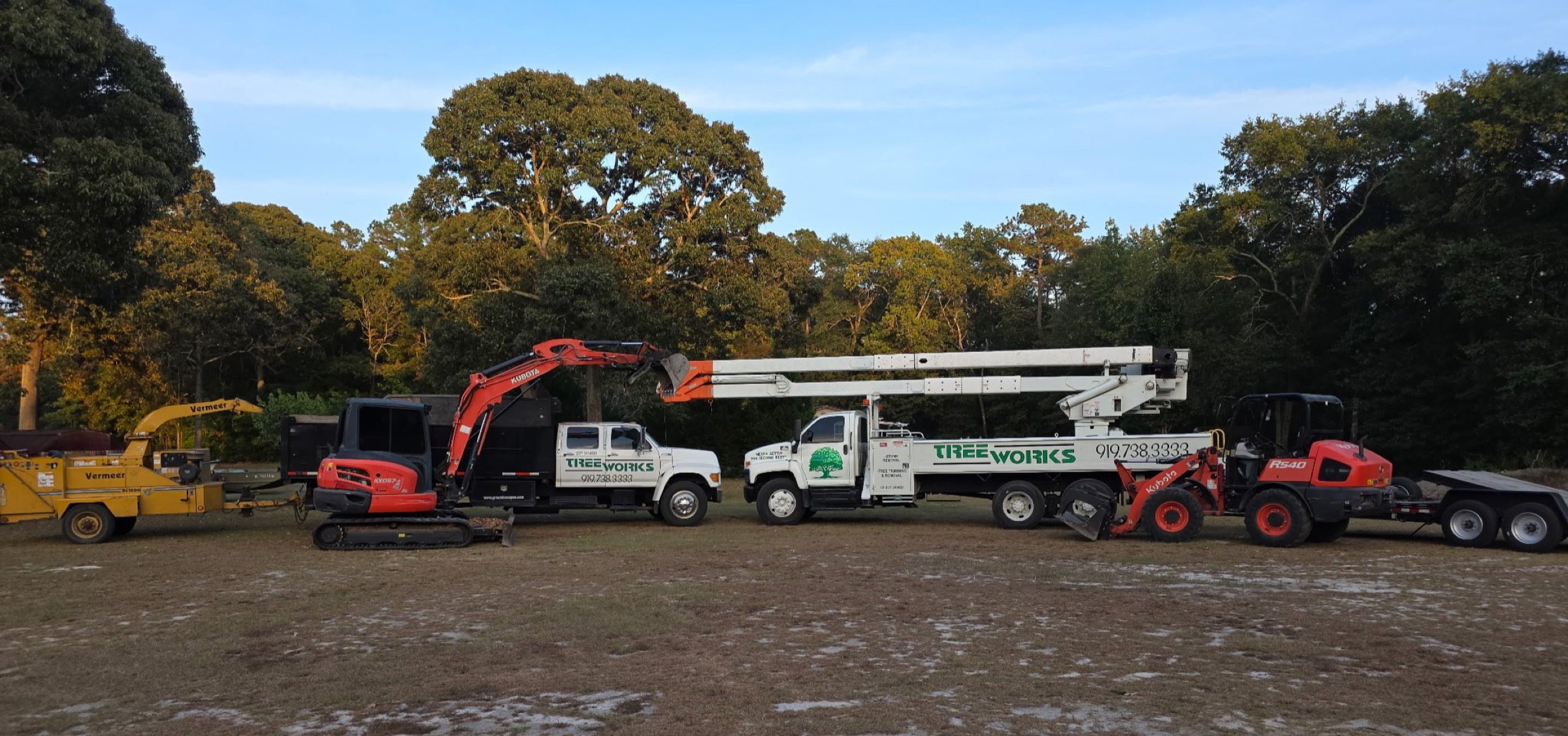 Tree Works fleet lined up: bucket truck, Kubota excavator, wood chipper, wheel loader and work truck